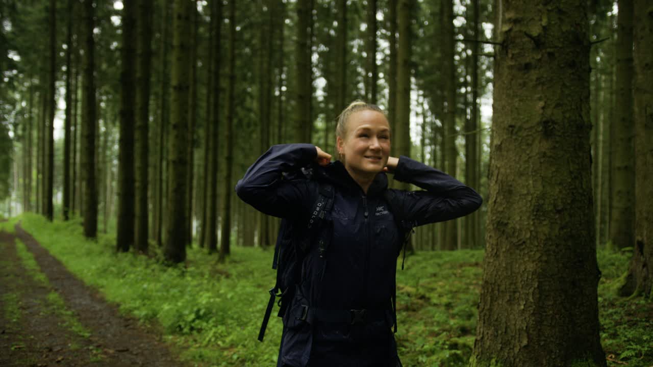 Glückliche Frau wandert im Regen durch einen Wald. Tief durchatmen im Wald. Von der Welt abschalten und einen Waldspaziergang genießen.