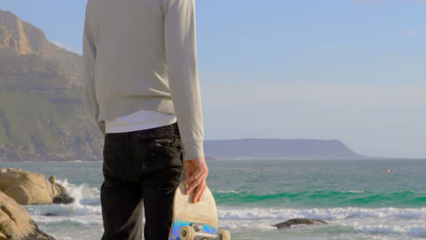 rear view of young caucasian man standing on the beach and looking at sea 4k