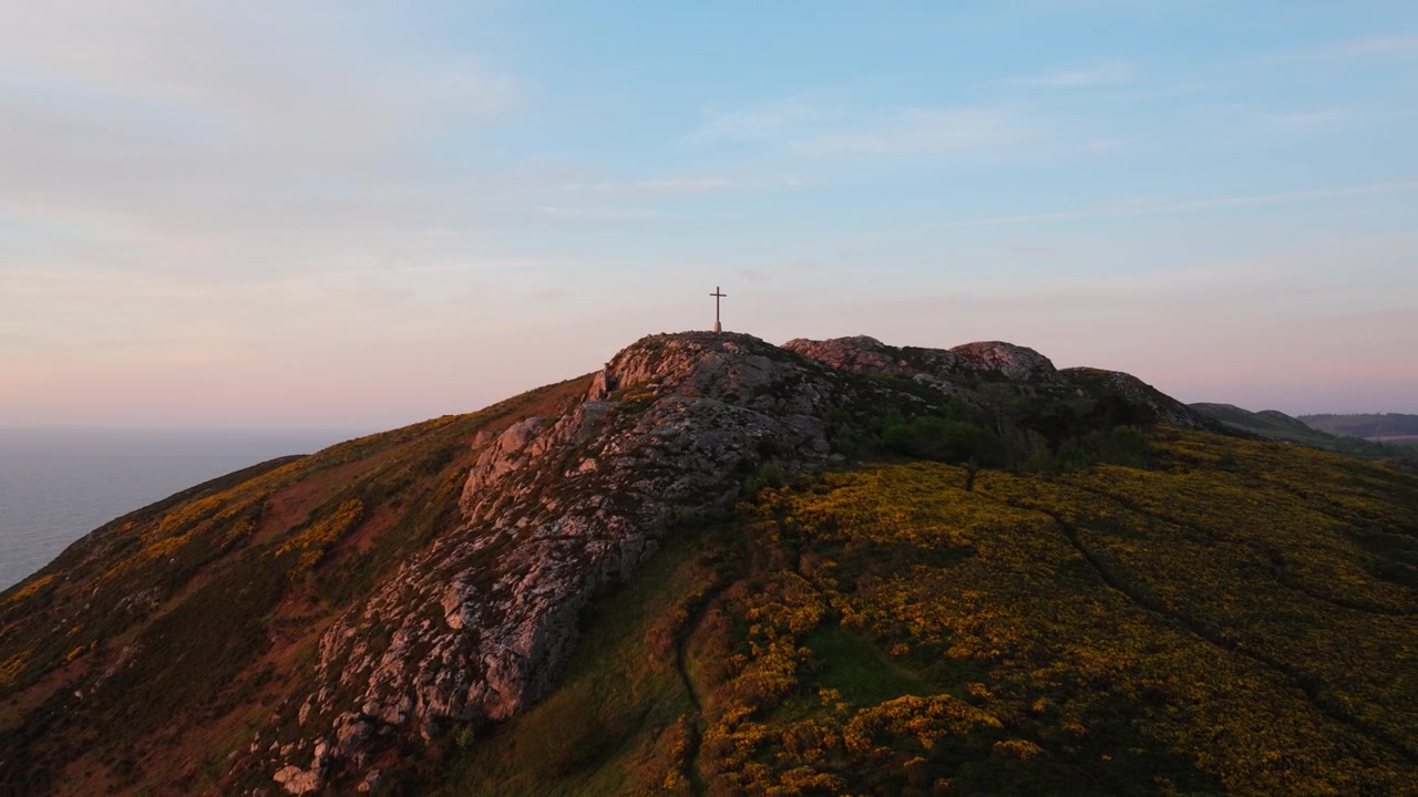 Una croce si erge su una collina rocciosa mentre il sole sorge, proiettando una luce calda sul paesaggio. Ideale per contenuti spirituali o di viaggio