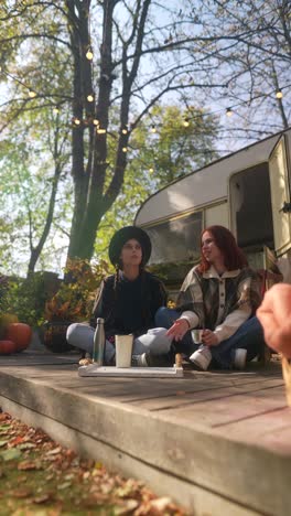 two friends enjoying autumn afternoon on a wooden deck with a campervan