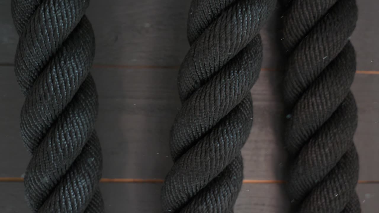 cuerdas de batalla de gimnasio profesionales colgadas en la pared con partículas de polvo o tiza moviéndose lentamente en el aire, cámara lenta