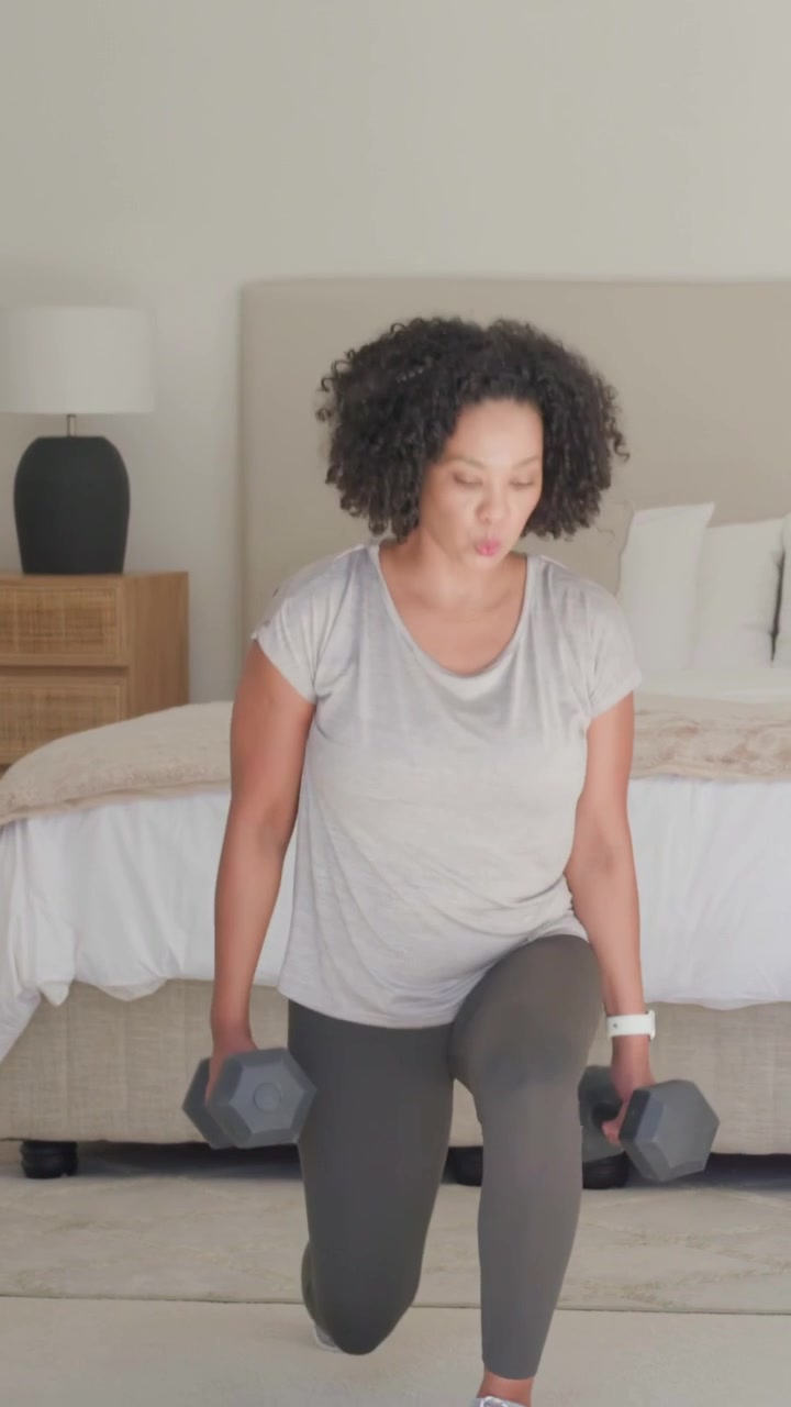 Video verticale: In pausa, una donna fa affondi camminando in camera da letto, in abbigliamento sportivo e con pesi esagonali per il fitness.
