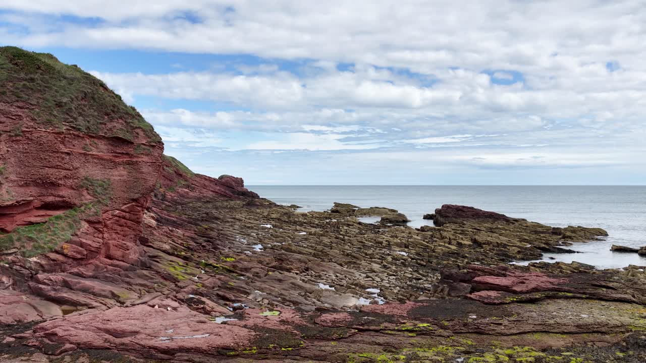 Camera slowly pans revealing red sandstone cliffs, layered rocks, and North Sea under soft daylight