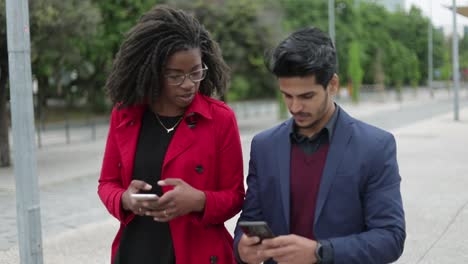 Woman-and-man-walking-along-street,-man-showing-photos-on-phone