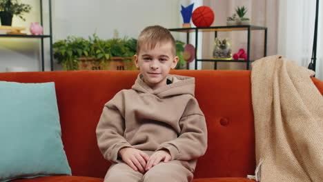 child kid boy smiling friendly at camera waving hands gesturing hello hi greeting at home on couch