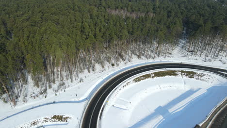 roads covered with snow, truck, and cars moving along the highway in a winter forest landscape in rakowice poland - aerial drone panning right shot from a fixed point