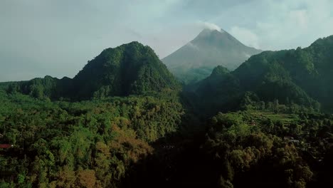 exuberantes colinas cubiertas de plantas en la jungla profunda de indonesia y volcán humeante en el fondo