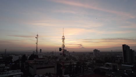 in the foreground a telecommunication antenna is seen in the background volcanoes are seen during a dawn in a city