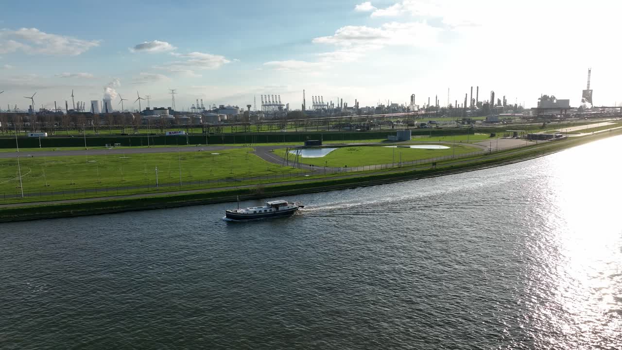 Semi orbit aerial shot of a passenger boat cruising Antwerp canal with wind turbines and industrial landscape in the background
