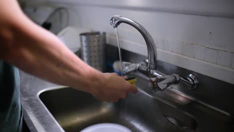 caucasian man washing dishes in stainless steel sink with yellow sponge