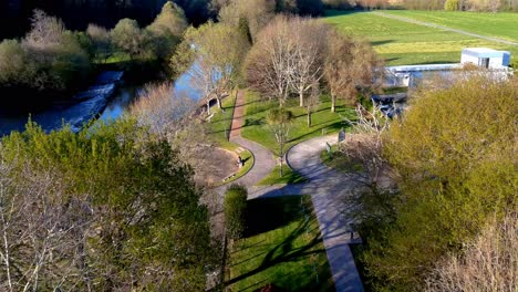 Aerial-Flying-Over-Praia-fluvial-de-Tapia-Park-Along-Rooftop-Of-Building-Next-To-Trees-With-No-Leaves