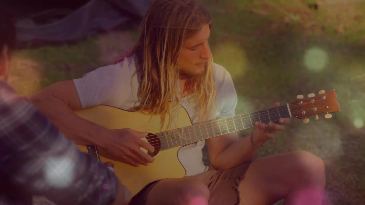 Musiker justerer guitarhals og begynder at slå akkorder an for ven, der lytter i solrig have.