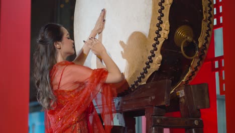 Beautiful-Asian-woman-wearing-a-traditional-red-Chinese-dress-beats-the-large-drum-to-celebrate-the-Chinese-new-Year---static-slow-motion