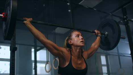 slow motion: training squats with barbells over head. muscular female lifting barbell over head training shoulders at gym. confident fitness woman practicing force workout with heavy equipment.