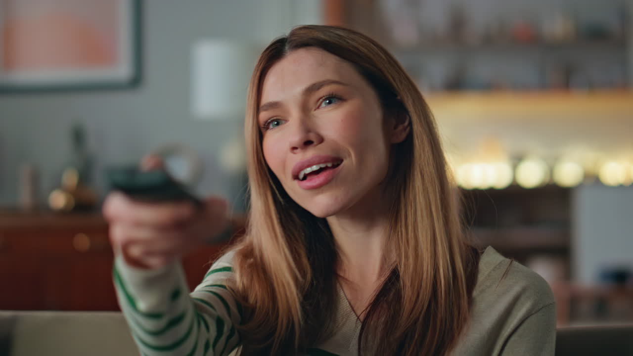 Closeup woman choosing television show pressing remote control on couch home