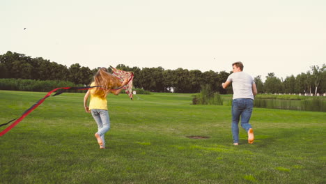 Feliz-Padre-E-Hija-Volando-Una-Cometa-Mientras-Corren-Juntos-En-El-Prado-En-Un-Parque