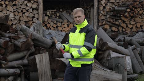 Lumberjack-in-reflective-jacket.-Man-woodcutter-hold-small-axe.-Sawn-logs,-firewood-background