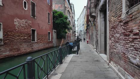 a slow-motion view of a narrow canal street in venice, italy, with brick buildings and a serene waterway along a cobblestone path