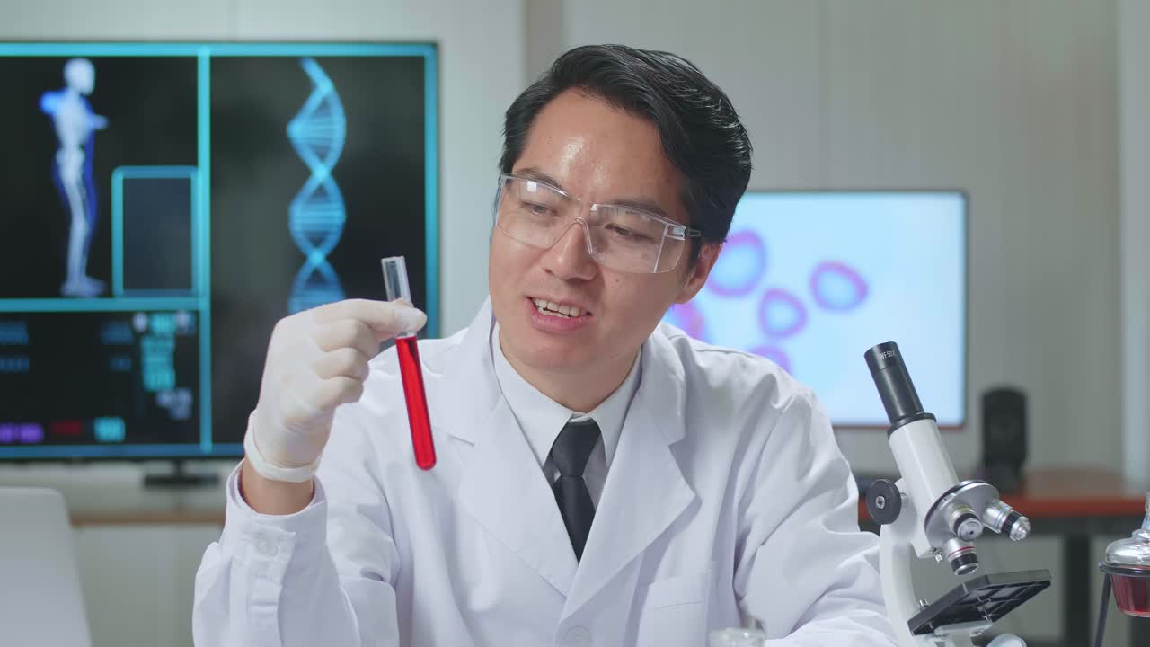 Young Asian Male Research Scientist Holding Glass Test Tube And Speaking To The Camera