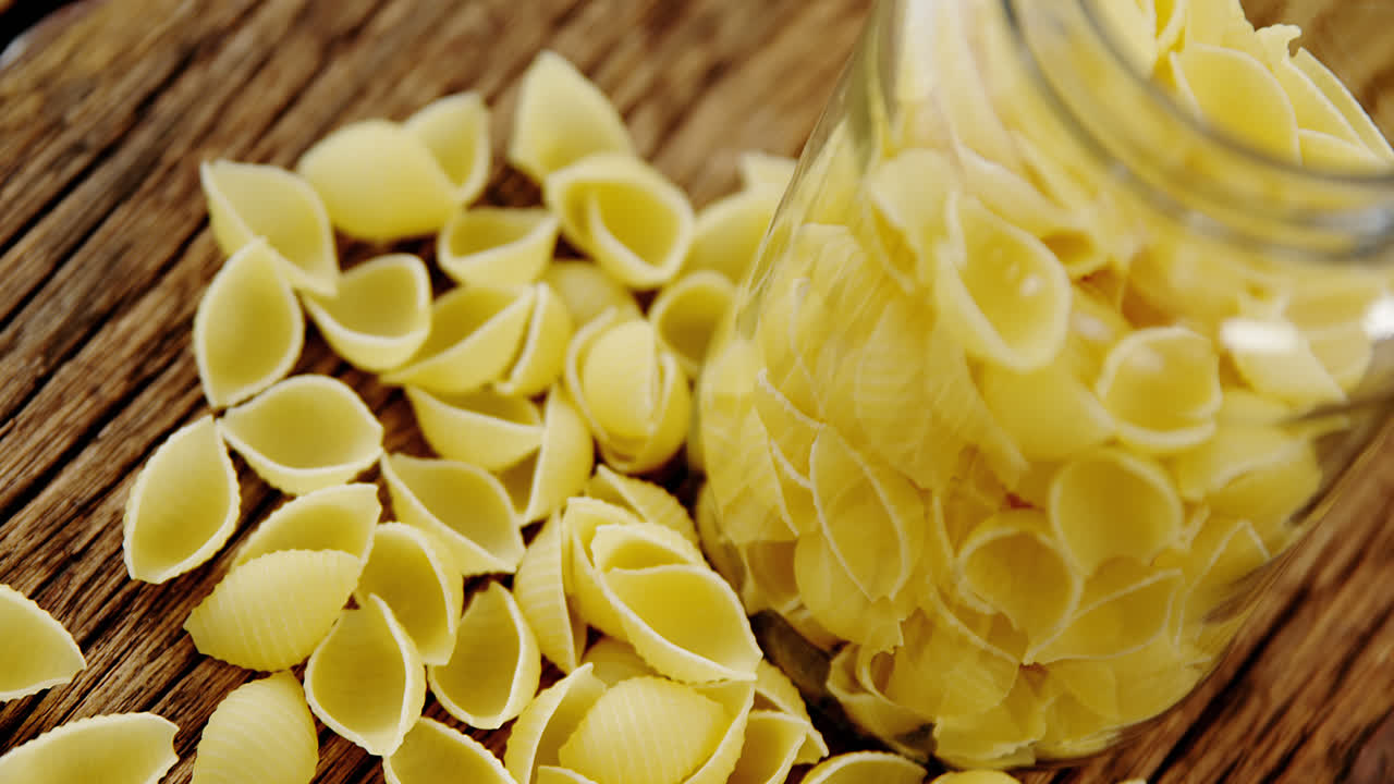 Scattered conchiglion pasta on wooden background and tidied in glass jar