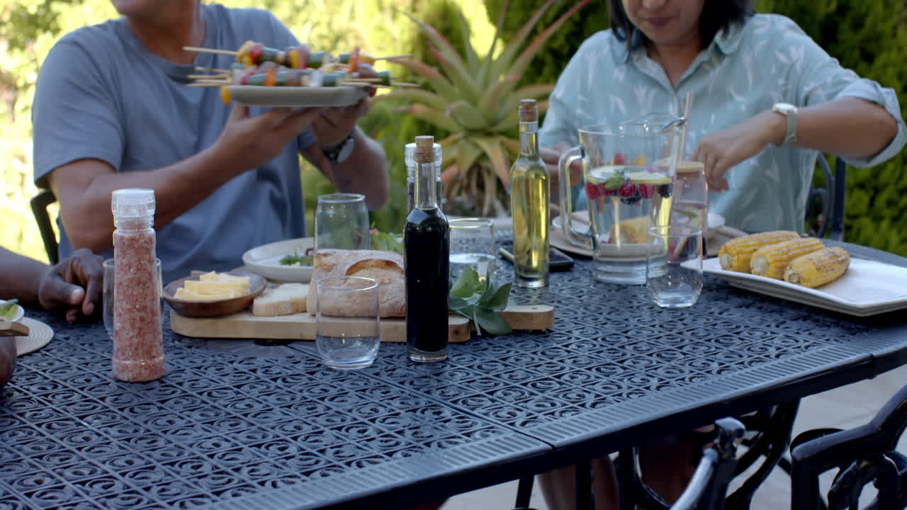 Enjoying in garden lunch, senior diverse friends sharing food and laughter at garden table