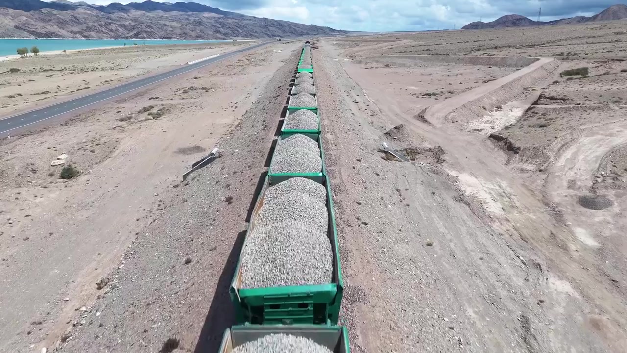 Vista aerea ravvicinata su un treno merci con ghiaia presso il bacino idrico di Orto Tokoy in Kirghizistan. Trasporti, industria.