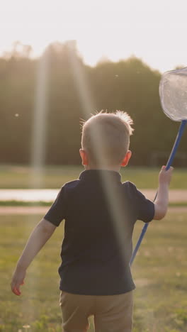 funny little boy runs holding hoop net along playground at sunset backside view slow motion. active game and nature. childhood time