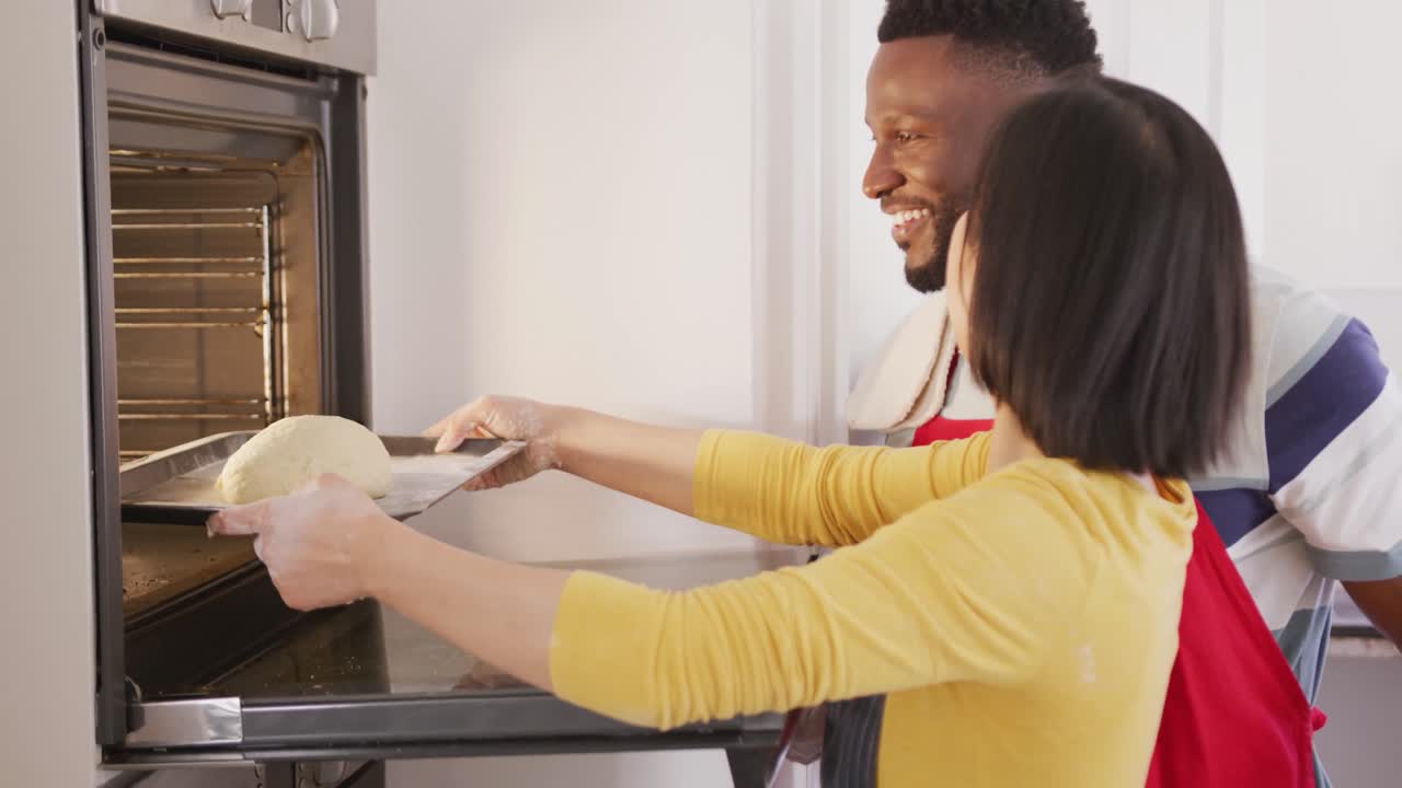 Felice coppia mista che indossa grembiuli e inforna il pane in cucina.