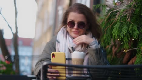 woman enjoying a latte and using phone in a cozy outdoor cafe