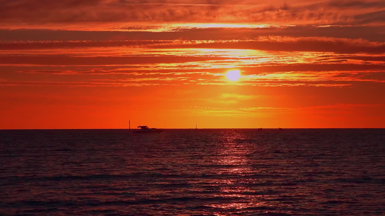 Breathtaking footage of a vivid sunset over a calm ocean, with the sky ablaze in rich hues of orange and red. The partially visible sun casts golden reflections