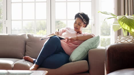 african american woman lounges on a sofa with a book at home