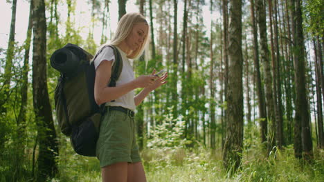 un viajero en el bosque con una mochila camina por el camino y mira la pantalla del teléfono móvil