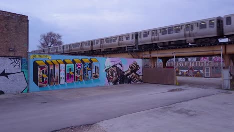 an rising aerial over a downtown chicago sign painted on a wall as an el train passes