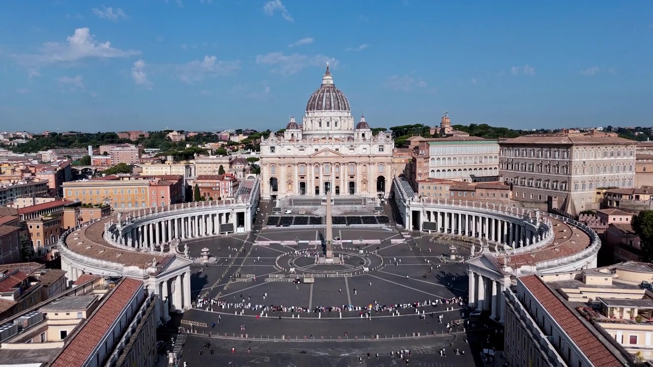Piazza San Pietro, elips şeklindeki sütunlu geçidi ve Aziz Petrus Bazilikası, ziyaretçiler açık meydanı geçerken berrak mavi gökyüzünün altında yer alıyor
