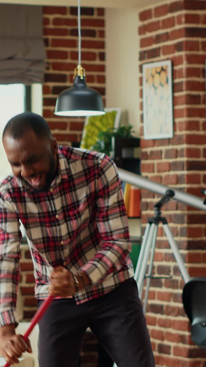 Vertical video: Cheerful man mopping apartment floors and listening to music