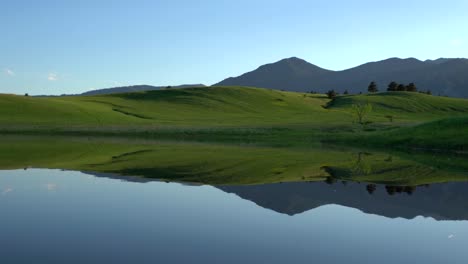 Reflexion-Von-Sanften-Hügeln-Und-Bäumen-Auf-Ruhiger-Wasseroberfläche