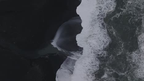 Aerial-top-view-of-ocean-waves-crashing-on-Iceland-Sólheimasandur-black-sand-beach,-on-a-moody-day