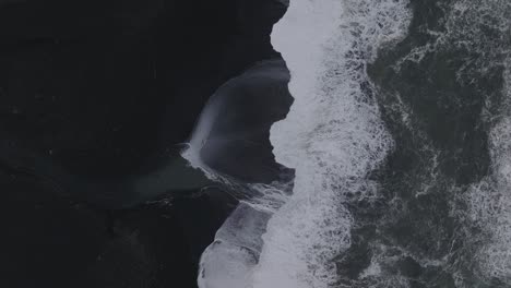 aerial top view of ocean waves crashing on iceland sólheimasandur black sand beach, on a moody day