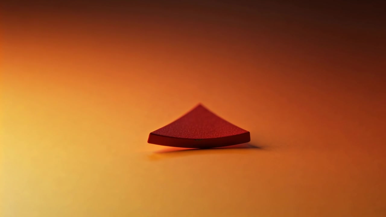 Dopo essere stato rilasciato, un cuneo rosso curvo cade ruotando su un tavolo arancione caldo, sistemandosi in posizione.