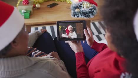 madre y hija afroamericanas usando una tableta para una videollamada de navidad con una mujer en la pantalla