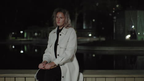 young girl sits near calm water at night, city lights reflecting, hand resting on book, lonely mood capturing thoughtful reflection in quiet urban environment with subtle architectural backdrop