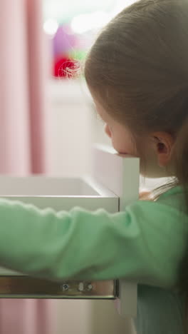 una niña curiosa abre el cajón del escritorio en la habitación de los niños. el niño busca artículos interesantes en el contenedor de la cómoda en casa. escolar y muebles domésticos