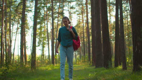 mujer excursionista caminando por un bosque tranquilo, llevando una bolsa roja sobre el hombro, la luz del sol se filtra a través de árboles altos, proyectando un brillo cálido y natural a través de la escena