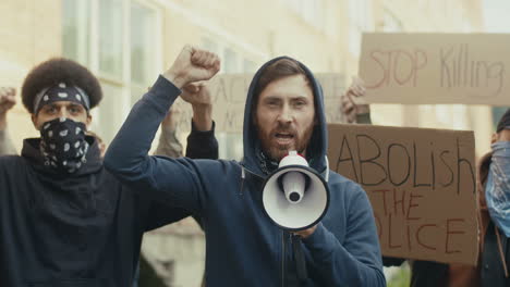 caucasian man yelling with arms up and talking on a loudspeaker in a protest with multiethnic group of people in the street