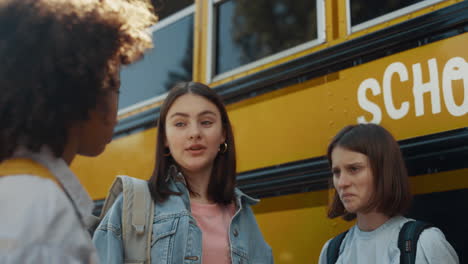 three school girls standing at yellow bus. diverse children talking in morning.