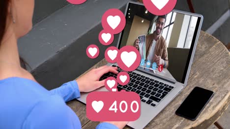Heart-icons-with-increasing-numbers-against-woman-having-a-video-call-with-man-on-laptop-at-home