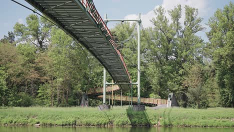 una toma de ángulo bajo de un puente colgante que atraviesa un río, rodeado de árboles verdes y cielos despejados