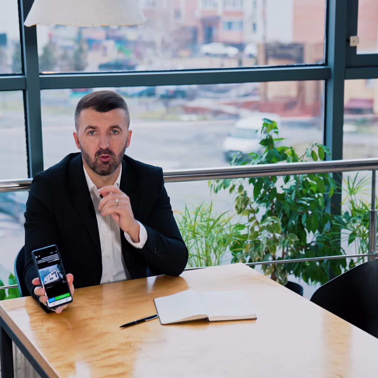 Bearded man in black suit sitting at the table. Businessman using phone searching for information and shows the result of search