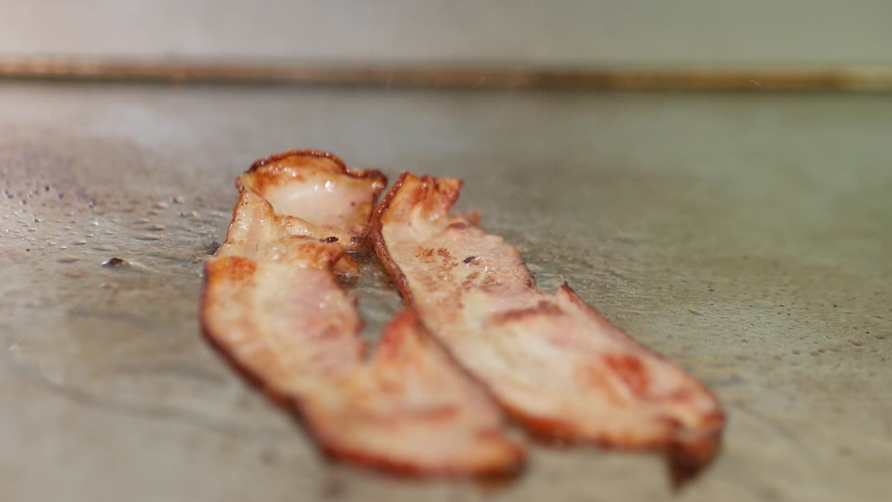 primer plano de tocino chisporroteando en una parrilla de un restaurante y volteado con pinzas