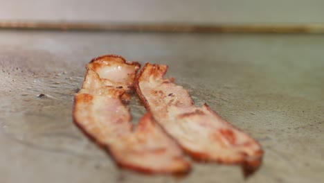 close-up of bacon sizzling on a restaurant grill and flipped with tongs